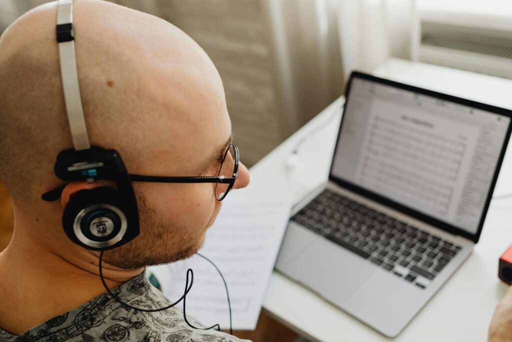 Person wearing headphones while reviewing songs on a laptop